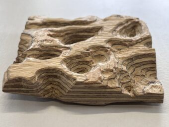 Topographic Relief Carved wood relief sculpture with layered topographic depressions and rounded recesses, shown from a low front angle against a white background.