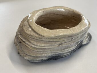 Layered Vessel Oval ceramic vessel sculpture made from stacked horizontal layers, with a glazed interior, raw textured exterior, and dark burn marks near the base.