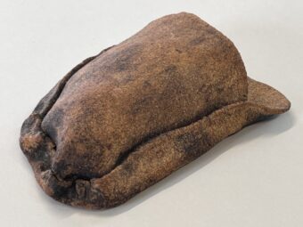 Earthen Fold Freeform ceramic sculpture with a folded, pouch-like shape, coarse unglazed surface, natural clay tones, and darkened edges from firing, shown from a low side angle.